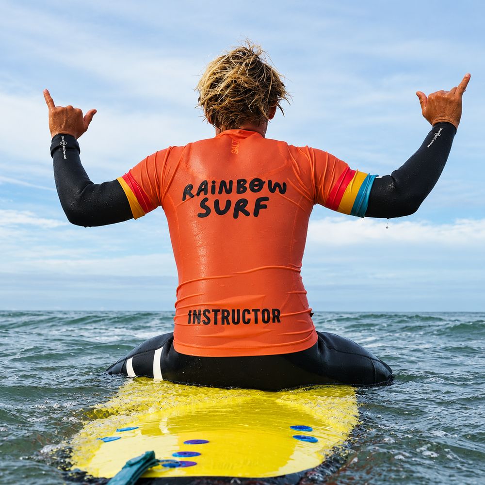 Instructor de Rainbow Surf sentado en su tabla haciendo shaka