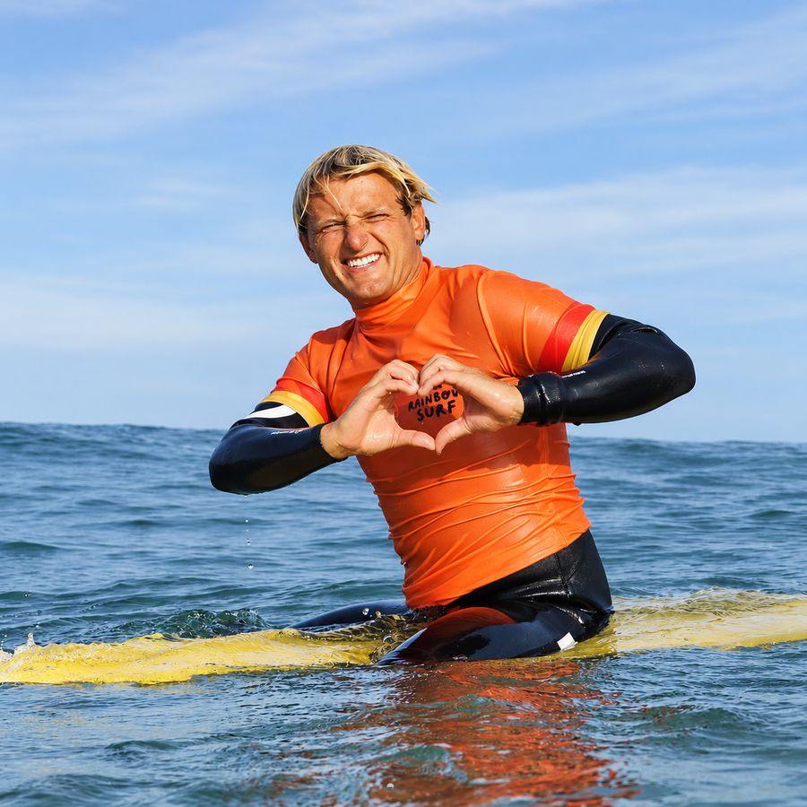 Instructor de Rainbow Surf haciendo un corazón con las manos en el agua